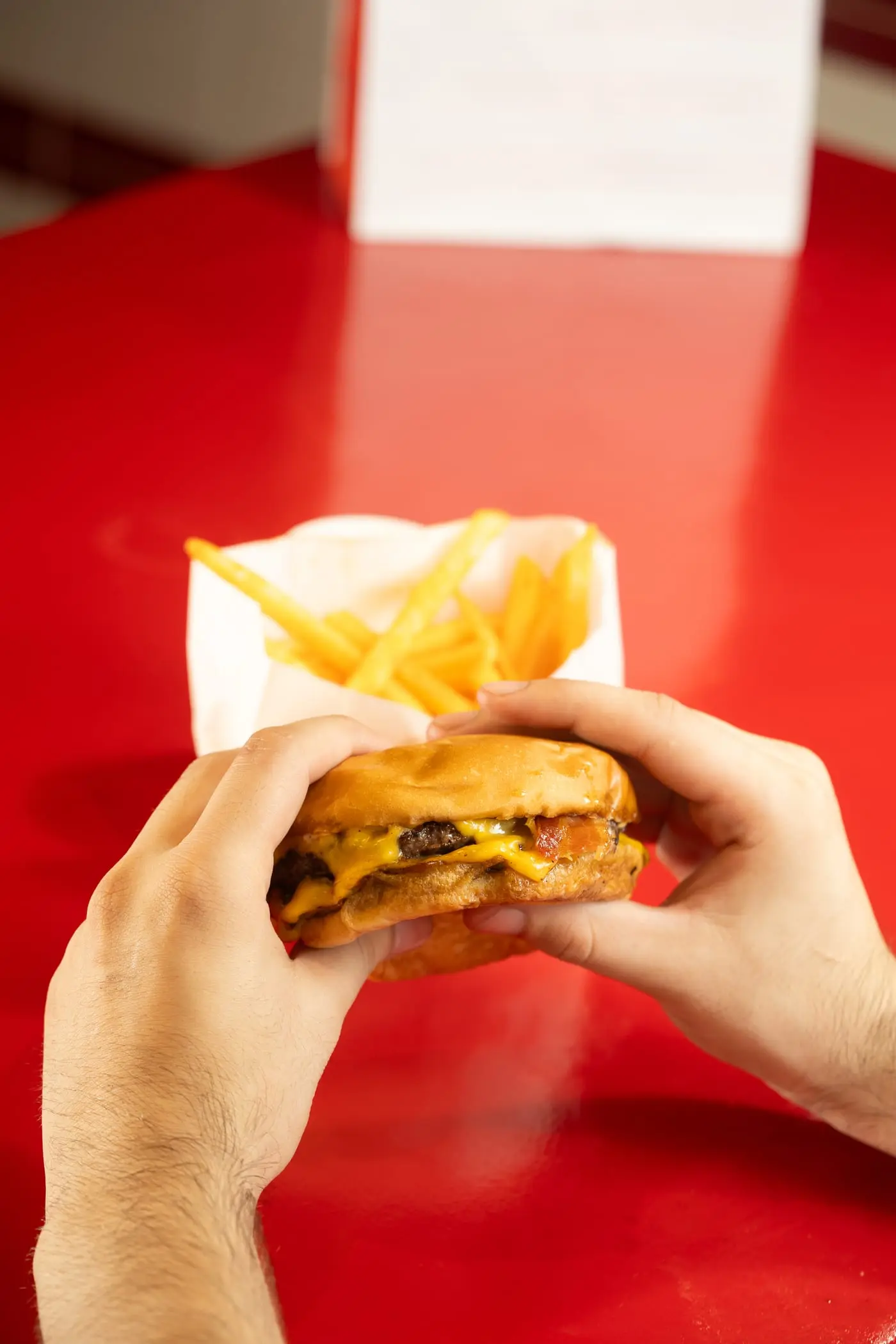 Manos sosteniendo una hamburguesa smash con una bolsa de papas fritas arriba